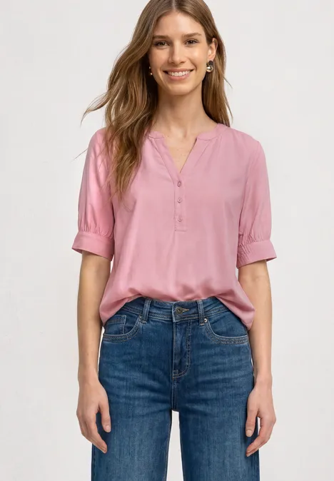 Blouse met korte mouwen, split in de hals en elastische zoom vintage blush Vrouw in roze blouse met V-hals en blauwe jeans, staand met handen langs het lichaam.
