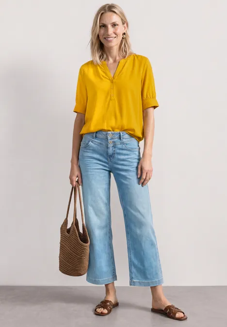 Blouse met korte mouwen, split in de hals en elastische zoom saffron yellow Vrouw met gele blouse, wijde blauwe jeans, bruine sandalen en gevlochten tas.