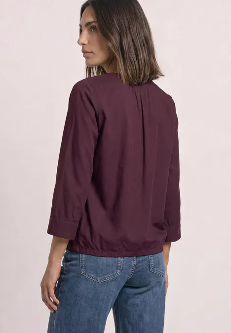 Blouse met 3/4-mouwen en split in de hals rustic rouge Vrouw in paarse blouse en spijkerbroek, schuin van achter gezien