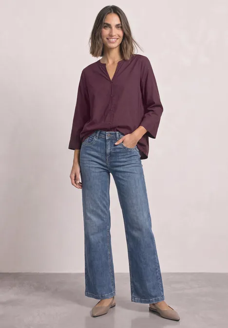 Blouse met 3/4-mouwen en split in de hals rustic rouge Vrouw in een paarse blouse en blauwe wijdvallende jeans tegen neutrale achtergrond.