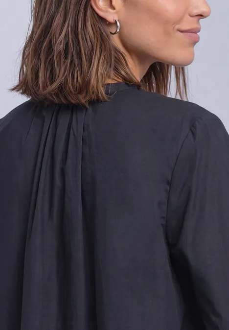 Femme aux cheveux bruns mi-longs et boucles d'oreilles argentées, vêtue d'un chemisier noir, vue de dos.