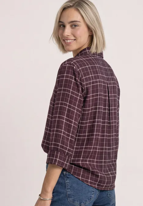Overhemdblouse met 3/4-mouwen en patroon rustic rouge Eine Frau dreht sich über die Schulter, trägt karierte Bluse und Jeans, lächelt.