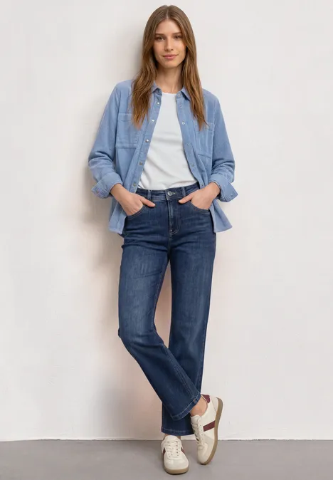 Corduroy overhemd met lange mouwen en knopen northern blue Frau trägt weißes T-Shirt, hellblaues Overshirt, dunkelblaue Jeans und helle Sneaker.