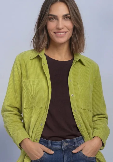 Corduroy overhemd met lange mouwen en knopen apple lime Frau mit grüner Hemdjacke, schwarzem Shirt und Jeans, lächelt in die Kamera.
