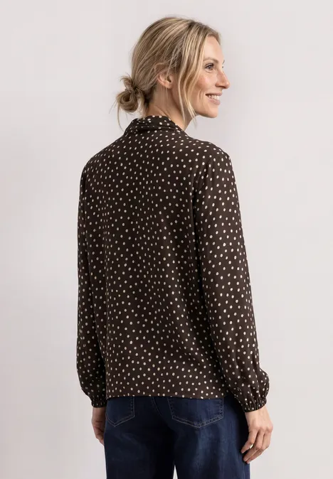Langarm Bluse mit Schleifendetail black coffee Frau im Profil trägt dunkle, gepunktete Bluse und Jeans, blondes Haar locker gebunden, vor hellem Hintergrund.
