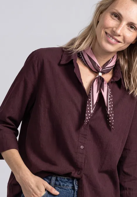 Overhemd met 3/4-mouwen en corduroy-mix rustic rouge Vrouw met lichtblond haar, bordeaux blouse en roze-bruin sjaaltje, vriendelijke glimlach.