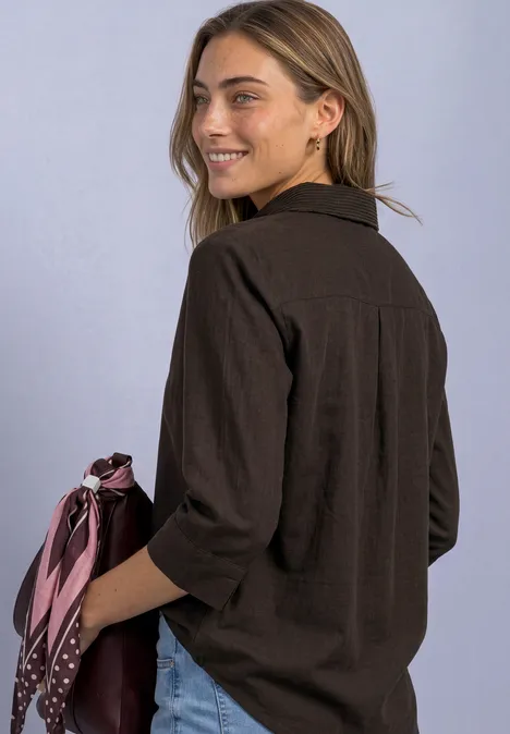 Overhemd met 3/4-mouwen en corduroy-mix black coffee Jonge vrouw in een zwart overshirt met opgestroopte mouwen, glimlacht zijwaarts en houdt een roze sjaal vast.