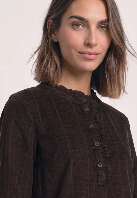 Portrait einer Frau in brauner Cordbluse mit Rüschenkragen und Knopfleiste.