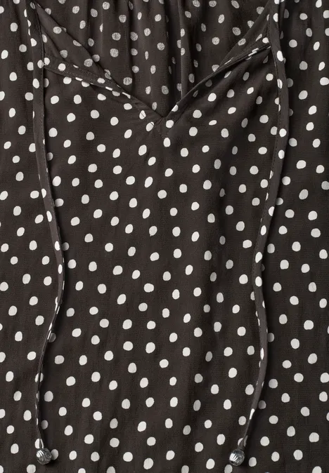 Schwarzes Kleidungsstück mit weißen Polka Dots und Kordelzug am Ausschnitt.