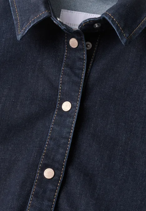 Nahaufnahme eines dunkelblauen Denim-Oberteils mit silbernen Druckknöpfen und kontrastierenden Nähten.