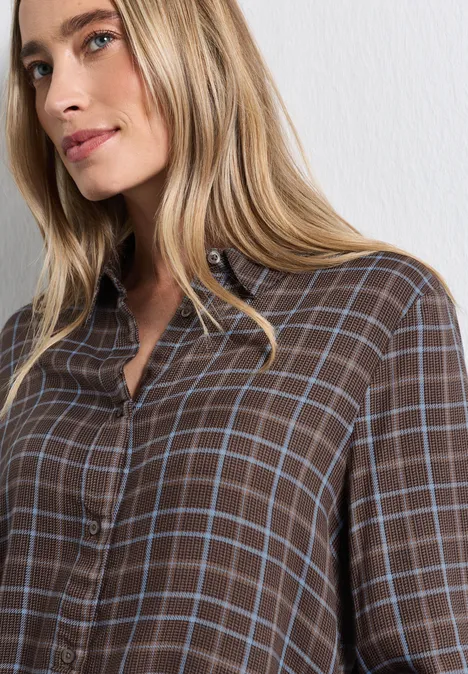 Eine blonde Frau trägt ein braunes, kariertes Hemd und blickt zur Seite.