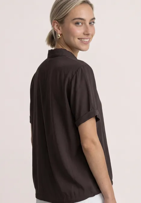 Overhemd met korte mouwen in effen kleur black coffee Eine lächelnde Frau im schwarzen Kurzarm-Shirt, seitlich stehend, die über die Schulter schaut.