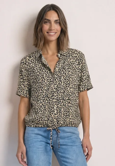 Kurzarm Hemdbluse mit Print cotton beige Frau trägt kurzärmliges, geknotetes Leoprint-Hemd und blaue Jeans, lächelnd vor neutralem Hintergrund.