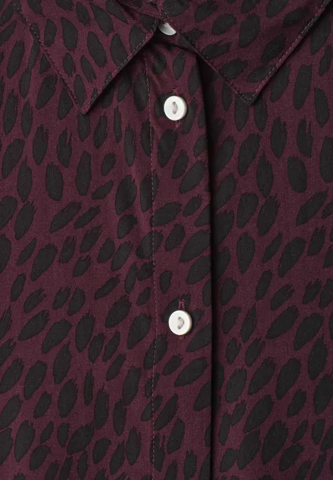 Nahaufnahme eines burgunderfarbenen Shirts mit schwarzem Blattmuster und weißen Perlmuttknöpfen.