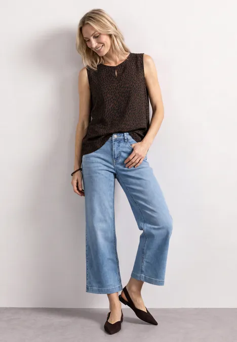 Frau trägt dunkelbraunes ärmelloses Top, weite hellblaue Culotte-Jeans und flache dunkle Schuhe.