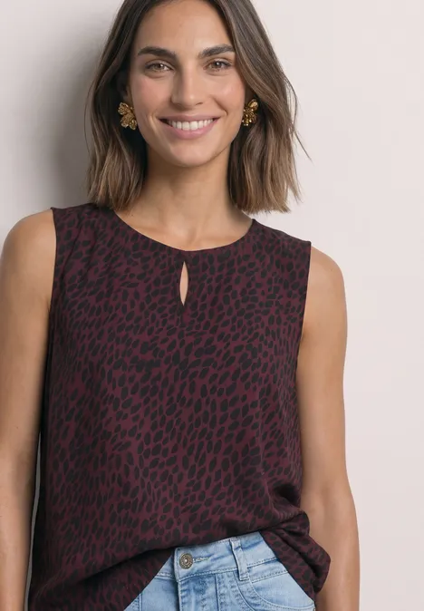 Vrouw lacht in een mouwloze bordeauxrode top met luipaardprint en een spijkerbroek.
