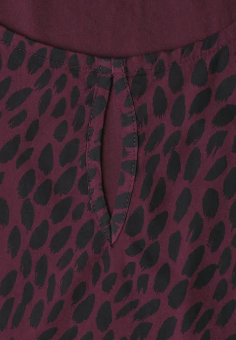Blouse van bordeaux stof met zwart bladmotief en een klein druppelvormig halsuitsnijdingsdetail