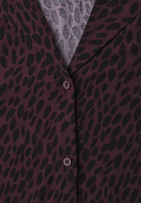Nahaufnahme eines lila Blazers mit schwarzem Blattmuster und Knöpfen.