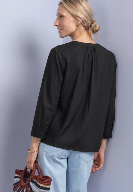 Blouse met 3/4-mouwen en split in de hals Black Vrouw van achteren in zwart overhemd, lichte spijkerbroek en met een gevlochten tas.