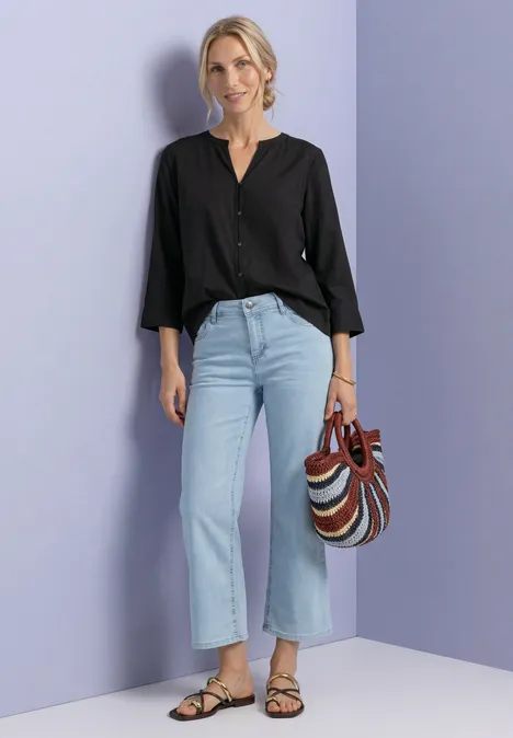Blouse met 3/4-mouwen en split in de hals Black Vrouw met zwarte blouse, lichtblauwe jeans, sandalen en gestreepte tas voor paarse achtergrond.