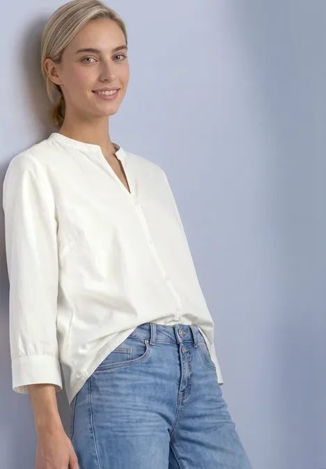 Blouse met 3/4-mouwen en split in de hals off white Eine junge Frau mit blonden Haaren trägt eine weiße Bluse und blaue Jeans vor hellem Hintergrund.