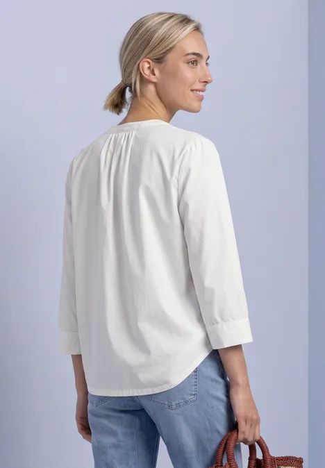 Blouse met 3/4-mouwen en split in de hals off white Frau von hinten in weißer 3/4-Arm-Bluse mit blondem Dutt, Jeans und kleiner brauner Tasche.