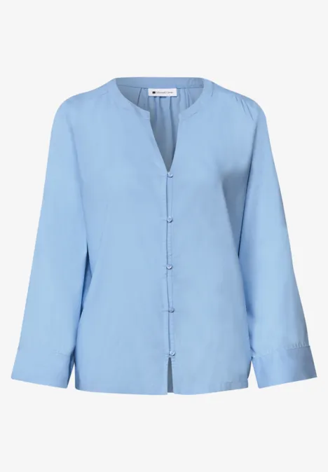 Chemisier bleu clair à manches longues, encolure en V et patte de boutonnage sur le devant.