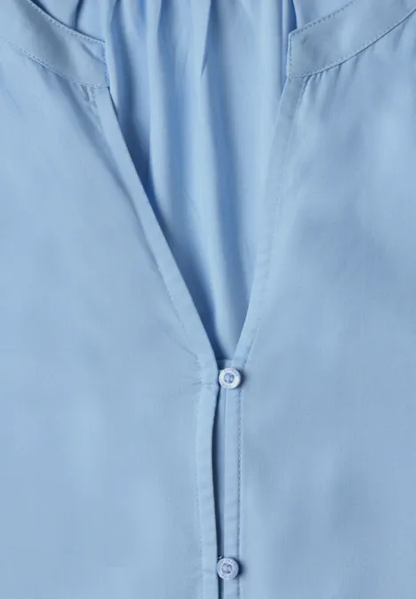 Chemise/blouse bleu clair vue en gros plan, légèrement ouverte à l'avant avec deux boutons apparents.