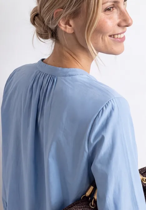 Vue de côté d'une femme souriante aux cheveux attachés portant un chemisier bleu clair.