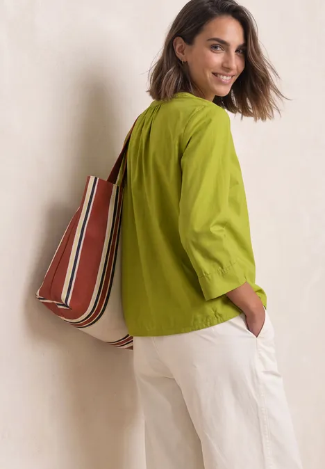 Blouse met 3/4-mouwen en split in de hals apple lime Vrouw met groene blouse, witte broek en gestreepte tas over haar schouder, glimlachend