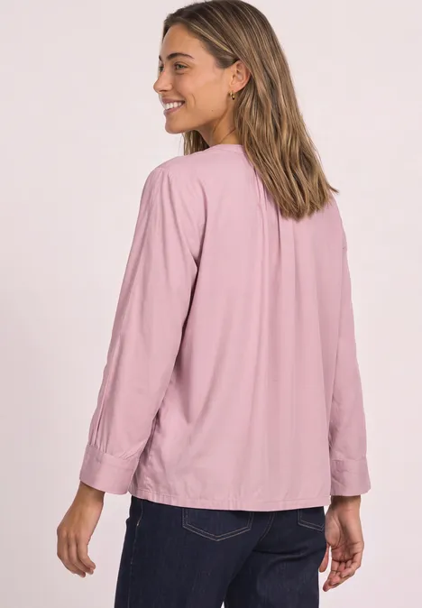 Une femme souriante en chemise rose et jean sombre regarde par-dessus son épaule.
