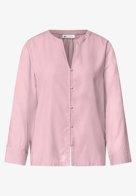 Chemisier rose pâle à manches longues, sans col, fermeture boutonnée et style épuré.