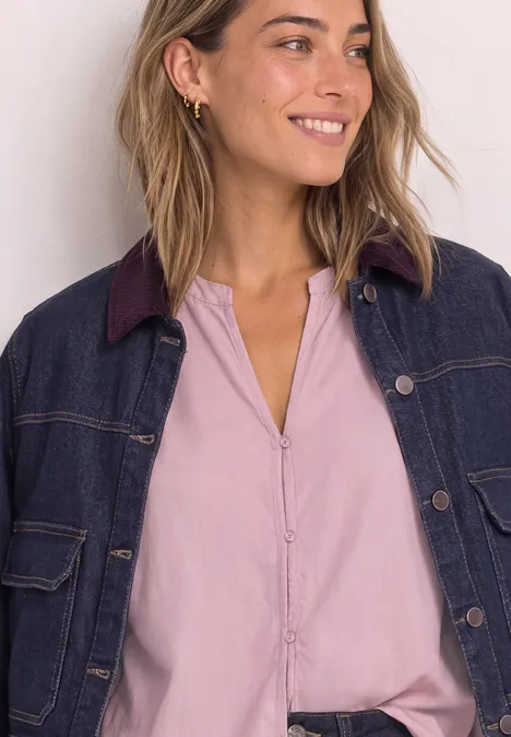 Jeune femme souriante portant un chemisier rose pâle et une veste en jean bleu foncé.