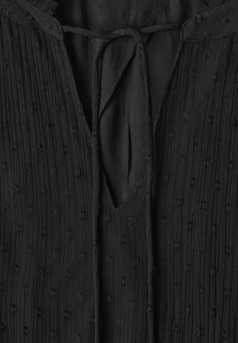 Schwarze Bluse mit geprägtem Punktemuster und V-Ausschnitt mit Bindeband.
