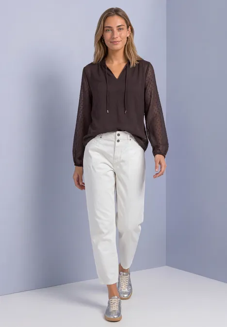 Chiffonblouse met split in de hals en bandjes ruby vine Vrouw in een donkeren blouse, witte high-waist pijpenbroek en zilveren schoenen voor een lila muur.