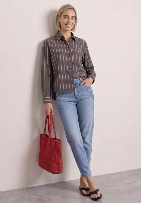 Langarm Hemdbluse mit Streifen espresso brown Frau lehnt an Wand, trägt gestreiftes Hemd, hellblaue Jeans, schwarze Sandalen und rote Tasche.