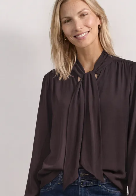 Blouse met lange mouwen en strikdetail ruby vine Frau in dunkelbrauner Schlupfbluse mit Kragen-Schleife und Jeans.