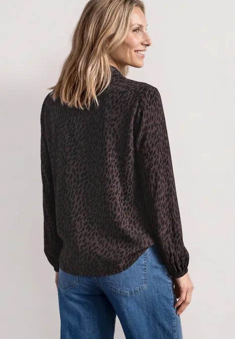 Langarm Bluse mit Schleifendetail molten earth Frau von hinten in dunkelbrauner Leoprint-Bluse und blauen Jeans vor hellgrauem Hintergrund.