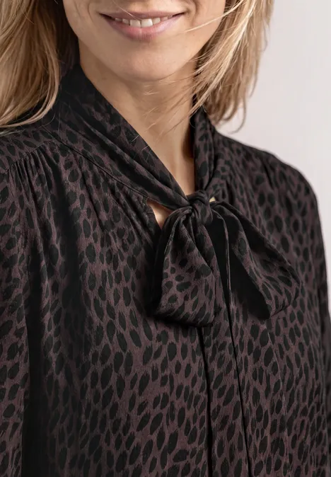 Langarm Bluse mit Schleifendetail molten earth Frau in schwarzer Bluse mit dezentem Leopardenmuster und Schleifenkragen.