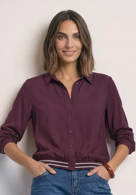 Overhemd met lange mouwen en elastische zoom rustic rouge Lächelnde Frau trägt bordeauxfarbenes Hemd und lässig die Hände in den Taschen.