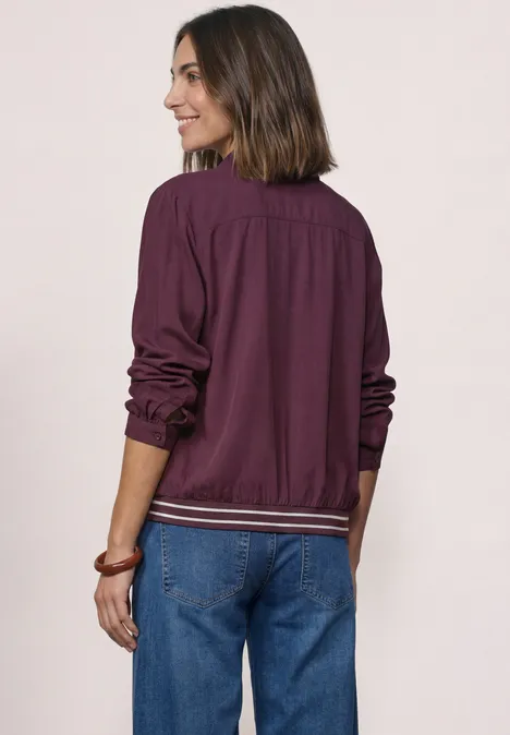 Overhemd met lange mouwen en elastische zoom rustic rouge Frau mit schulterlangen Haaren, lila Jacke und blauen Jeans, lächelt und steht vor hellem Hintergrund.