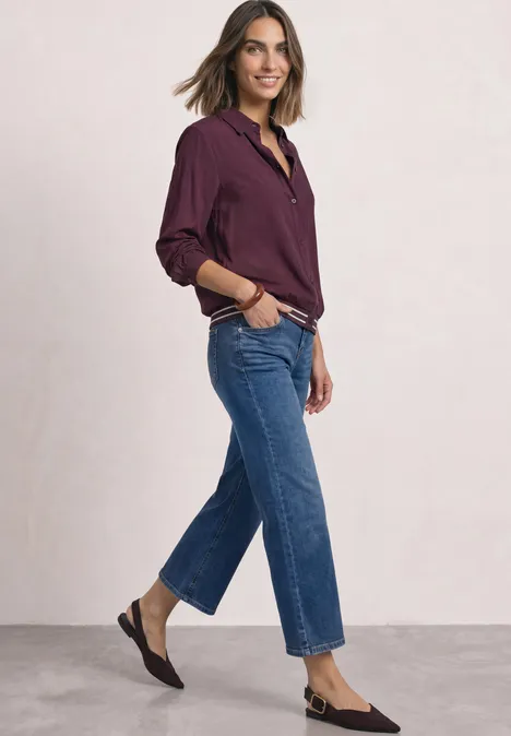 Overhemd met lange mouwen en elastische zoom rustic rouge Frau in lässiger Jeans, burgunderfarbener Bluse und flachen Schuhen, die lächelnd seitlich posiert.