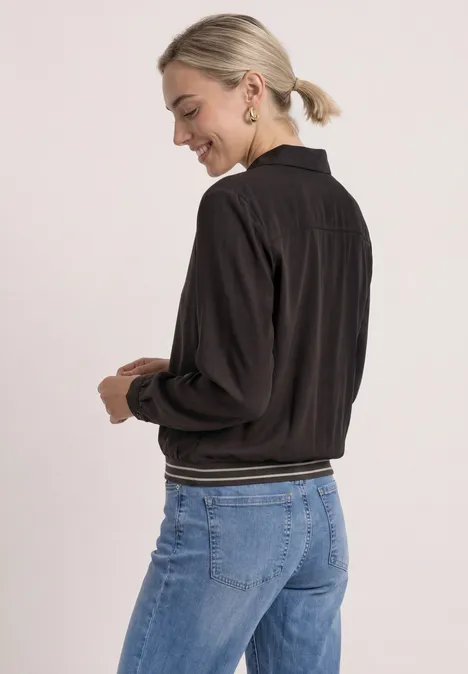 Overhemd met lange mouwen en elastische zoom black coffee Frau von hinten in schwarzer Bomberjacke und blauen Jeans, lächelnd, Haare im Pferdeschwanz.