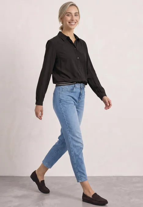 Overhemd met lange mouwen en elastische zoom black coffee Eine lächelnde Frau in schwarzer Bluse, hoch geschnittenen blauen Jeans und braunen Loafers vor hellem Hintergrund.