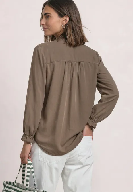 Blouse met 3/4-mouwen, split in de hals en ruches saddle brown Frau im Profil trägt lässige braune Bluse, weiße Hose und eine gestreifte Tasche.