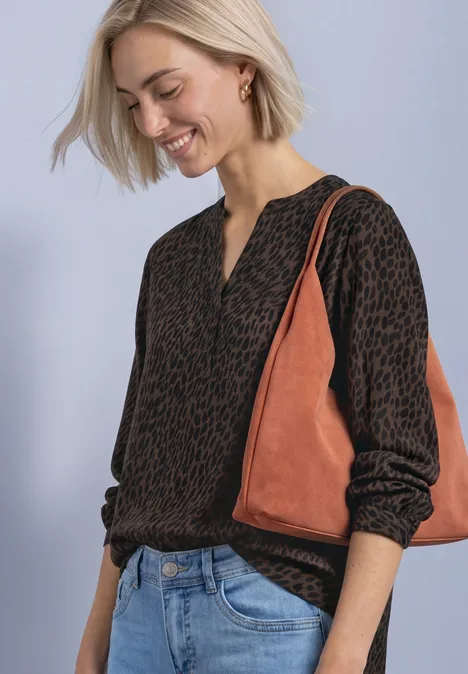 Langarm Bluse mit Split Neck und Print molten earth Eine Frau in gemustertem Pullover, Jeans und braun-orangener Tasche lächelt und blickt nach unten.