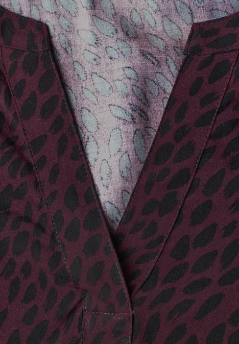 Blouse met lange mouwen, split in de hals en print rustic rouge Close-up van bordeauxrode stof met zwarte bladprint en lichtblauwgrijze binnenvoering.