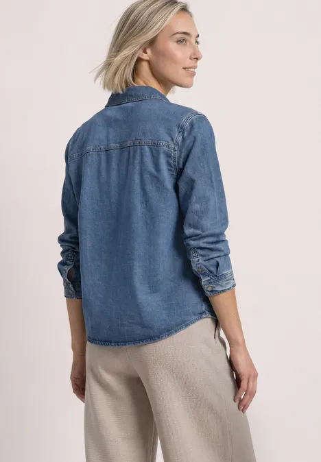 Overhemd met lange mouwen en borstzakken Medium Blue Soft washed Frau im Profil mit blauer Jeansbluse und beiger Hose vor neutralem Hintergrund.