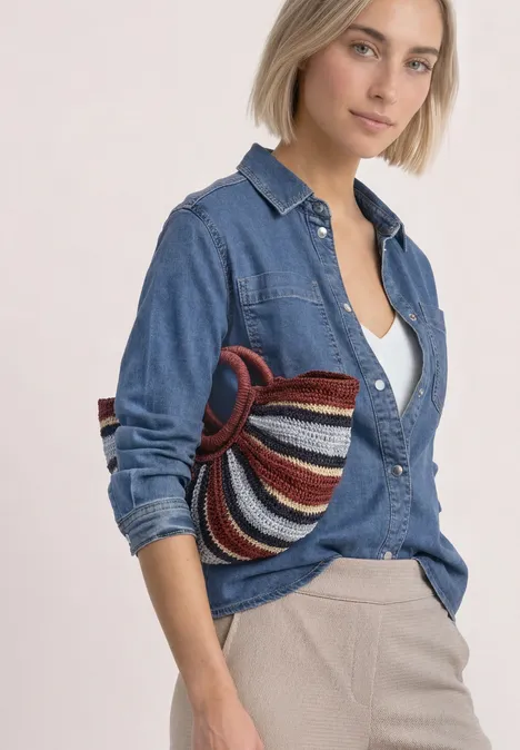 Overhemd met lange mouwen en borstzakken Medium Blue Soft washed Frau trägt Jeanshemd und helle Hose, hält bunt gestreifte Tasche lässig unter dem Arm.