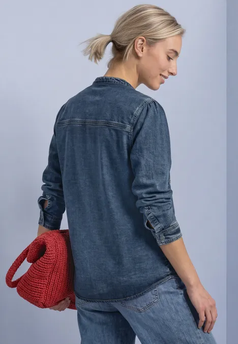 Blouse met lange mouwen en borstzakken Medium Blue Soft washed Frau von hinten in dunkelblauem Jeanshemd und Jeanshose, trägt eine rote Tasche, Haare im Pferdeschwanz.